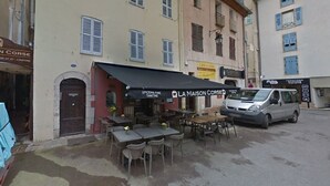 Un café avec une terrasse, un fourgon garé et un bâtiment doté de nombreuses fenêtres et volets.