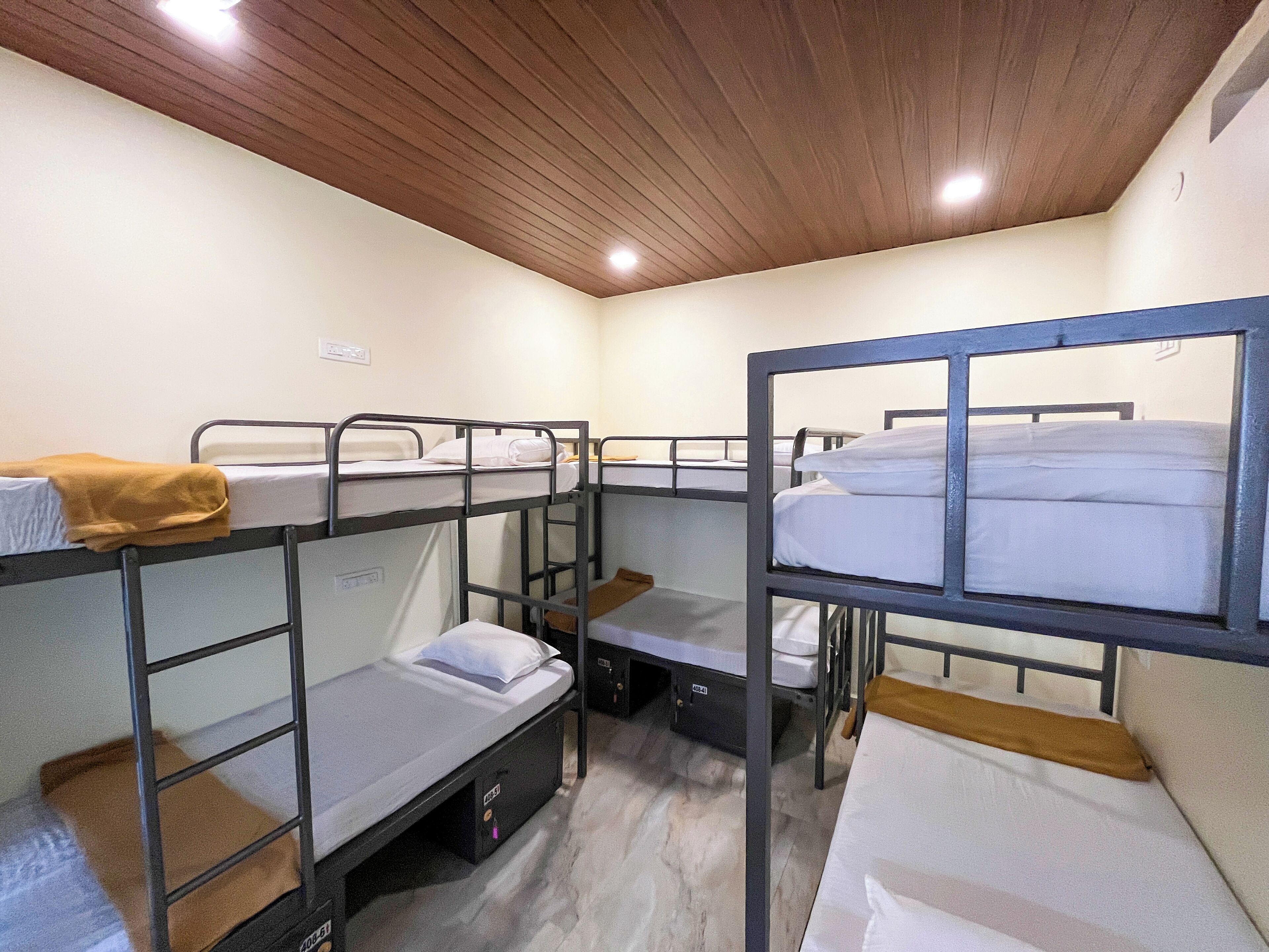 Une chambre de dortoir avec des lits superposés, un plafond en bois et un mur blanc.