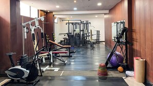 A gym with various exercise equipment, including a treadmill, weight machines, and a wall-mounted exercise bike. - Ananya Dorms (Hospet)
