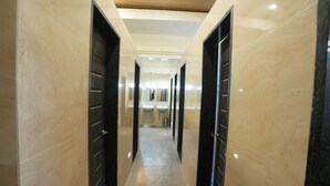 A corridor with marble walls and black doors, leading to a bathroom area with sinks and mirrors. - Ananya Dorms (Hospet)