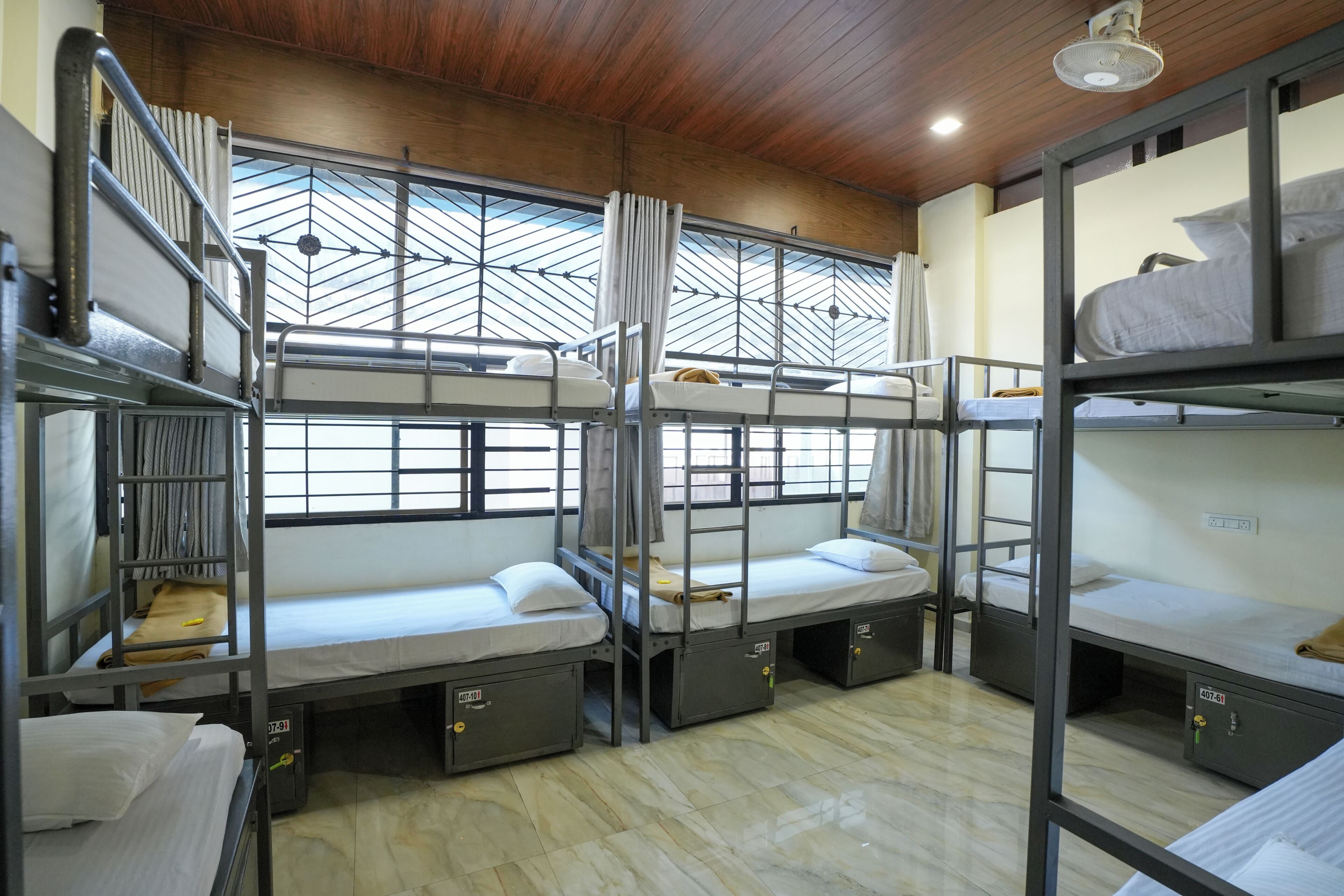 A bunk bed room with metal railings, a wooden ceiling, and a window with a geometric pattern.