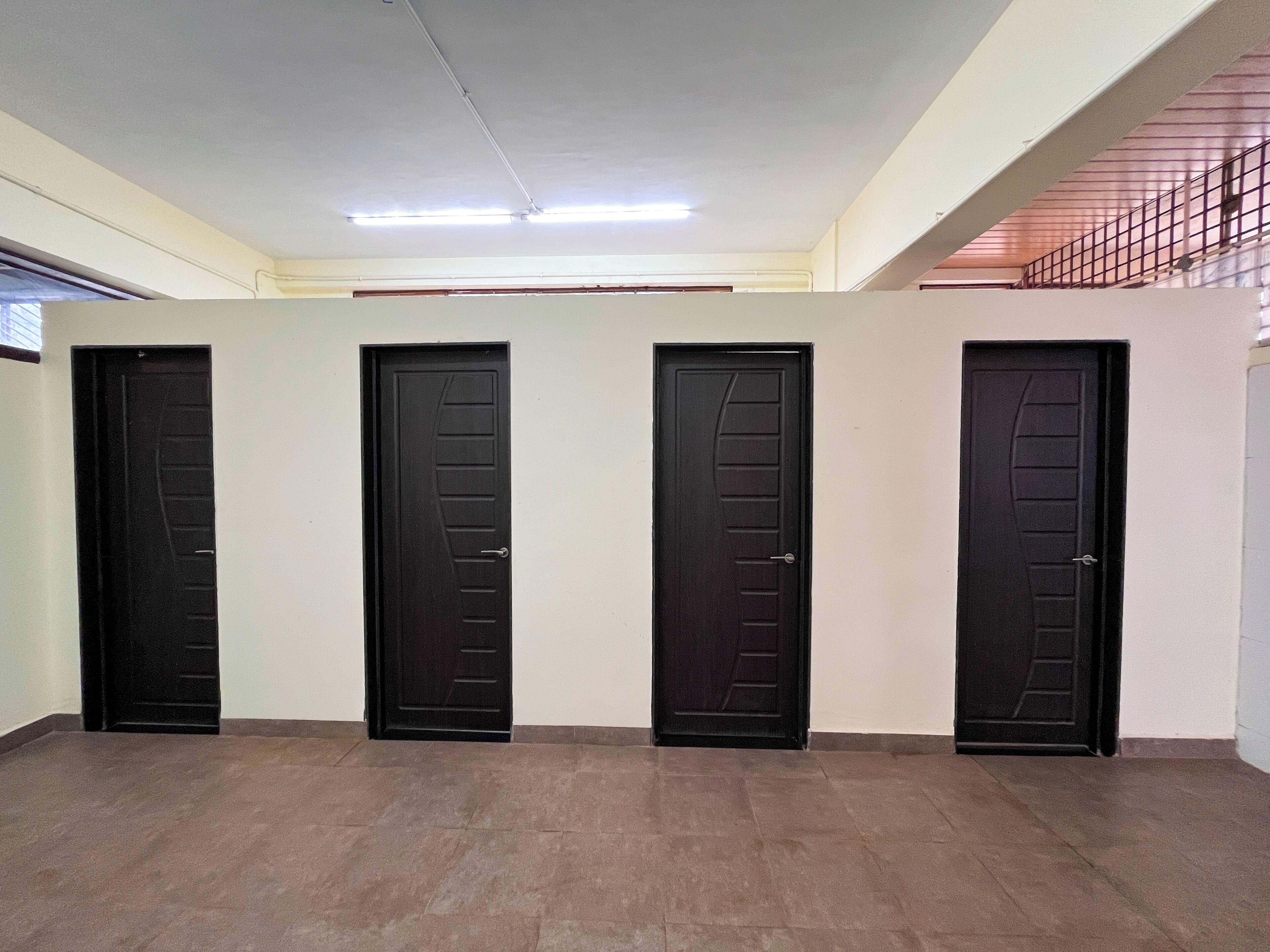 Un couloir avec quatre portes noires, un sol carrelé et un plafond éclairé par des néons.