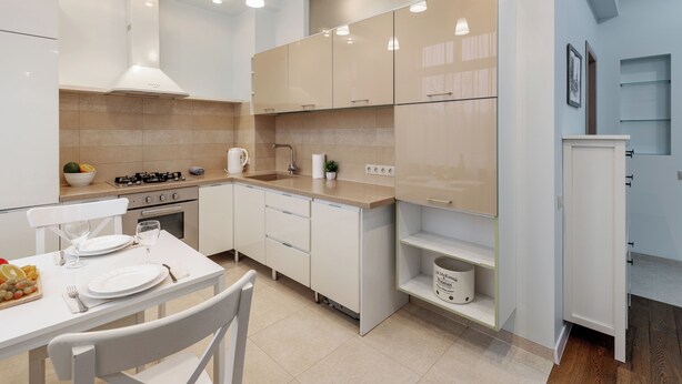 A modern kitchen with white cabinets, a gas stove, and a dining area with a table set for two. - Lux apartment with view on Svisloch (Minsk)