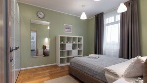 A bedroom with a bed, bedside tables, a white wardrobe, a mirror, a shelf with plants, and a window with curtains. - Lux apartment with view on Svisloch (Minsk)