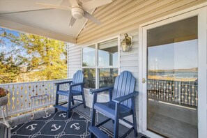 A covered porch with two blue Adirondack chairs, a ceiling fan, and a view of the water.