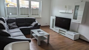 Een moderne woonkamer met een modulaire bank, een witte fauteuil, een salontafel, een televisie en een inbouwmeubel.