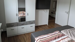 Een slaapkamer met een bed, een kledingkast, een televisie en een badkamer is op de achtergrond zichtbaar.