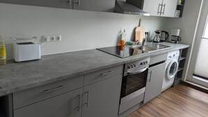 Een moderne keuken met grijze kastjes, een ingebouwde oven, een wasmachine en een aanrecht met een broodrooster en een koffiezetapparaat.