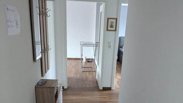 Een gang met houten vloer, een spiegel en een metalen rek met een wit voorwerp erop.