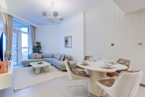 A modern living room with a sofa, a dining table set for four, and a large window providing natural light.