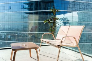 Ein moderner Außenbereich mit Sitzgelegenheit, einem Glastisch, einem gepolsterten Stuhl, einem Blumentopf und Blick auf ein Glasgebäude.