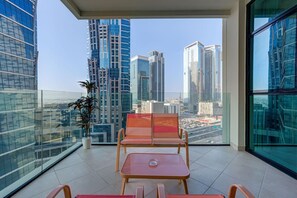 A balcony with a view of tall buildings, a potted plant, and seating area with a table.