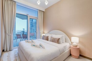A hotel room with a large bed, a bedside table with a lamp, and a view of a balcony with chairs and a plant.