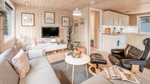 Una sala de estar acogedora con un sofá, un sillón de cuero, una mesa de centro y un televisor. Hay una zona de cocina con armarios y un lavabo.