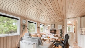 Un interior de cabaña acogedor con techo de madera, un sofá, una mesa de comedor y un televisor.