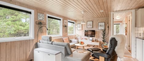 A cozy cabin interior with a wooden ceiling, a sofa, a dining table, and a TV.
