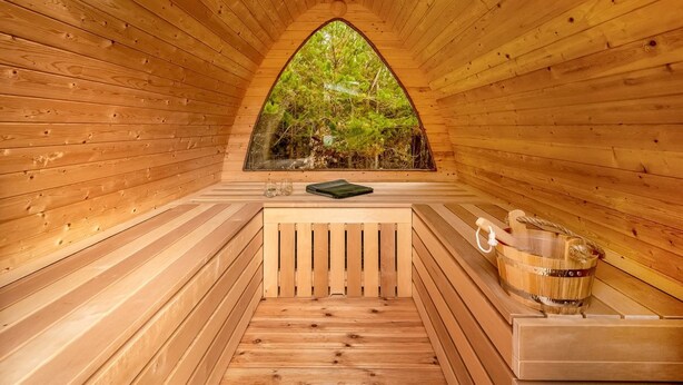 Una sauna de madera con vistas a árboles a través de un ventanal triangular.