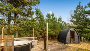 Una terraza de madera con un jacuzzi y una pequeña estructura tipo cabaña.