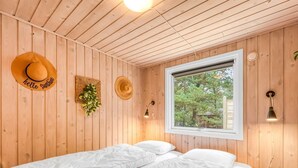Habitación acogedora con paredes de madera, una cama con ropa de cama blanca, una ventana con vistas a árboles y dos lámparas fijadas a la pared.