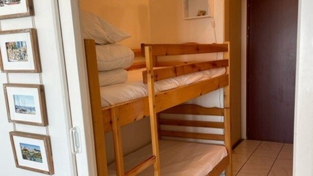 A bunk bed with white bedding in a room with tiled flooring and framed pictures on the wall.