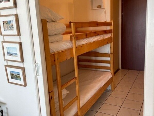 A bunk bed with white bedding in a room with tiled flooring and framed pictures on the wall.