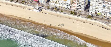 An aerial view of a coastal area with buildings along the beach and waves crashing onto the shore.