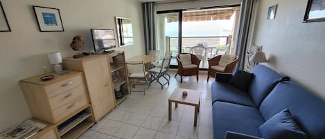 Un salon compact avec un canapé bleu, un meuble en bois, une petite table et un balcon équipé de chaises.