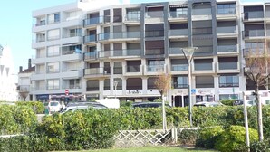 Un edificio residencial de varios pisos con balcones, un estacionamiento y una calle frente a él.