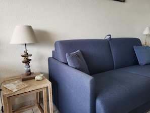 Ein blaues Sofa mit Kissen, ein kleiner Holztisch mit Lampe und ein Buch.