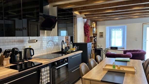 Una cocina moderna con armarios negros, una mesa de comedor de madera y una zona de estar acogedora con un sofá púrpura.