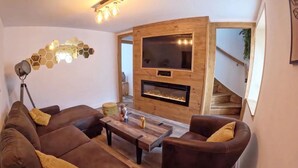Una sala de estar moderna con un conjunto de sofá, una mesa de centro, una chimenea y un televisor montado en una pared de madera.
