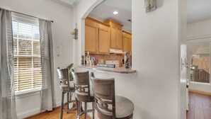 A kitchen with wooden cabinets, a countertop with a motivational sign, and a window with blinds.