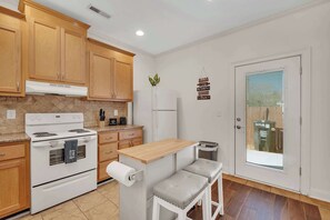 A kitchen with wooden cabinets, a white stove, a refrigerator, a small wooden table, and a bench.