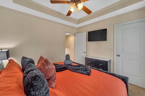 A bedroom with a bed, a ceiling fan, a TV, and a fireplace.