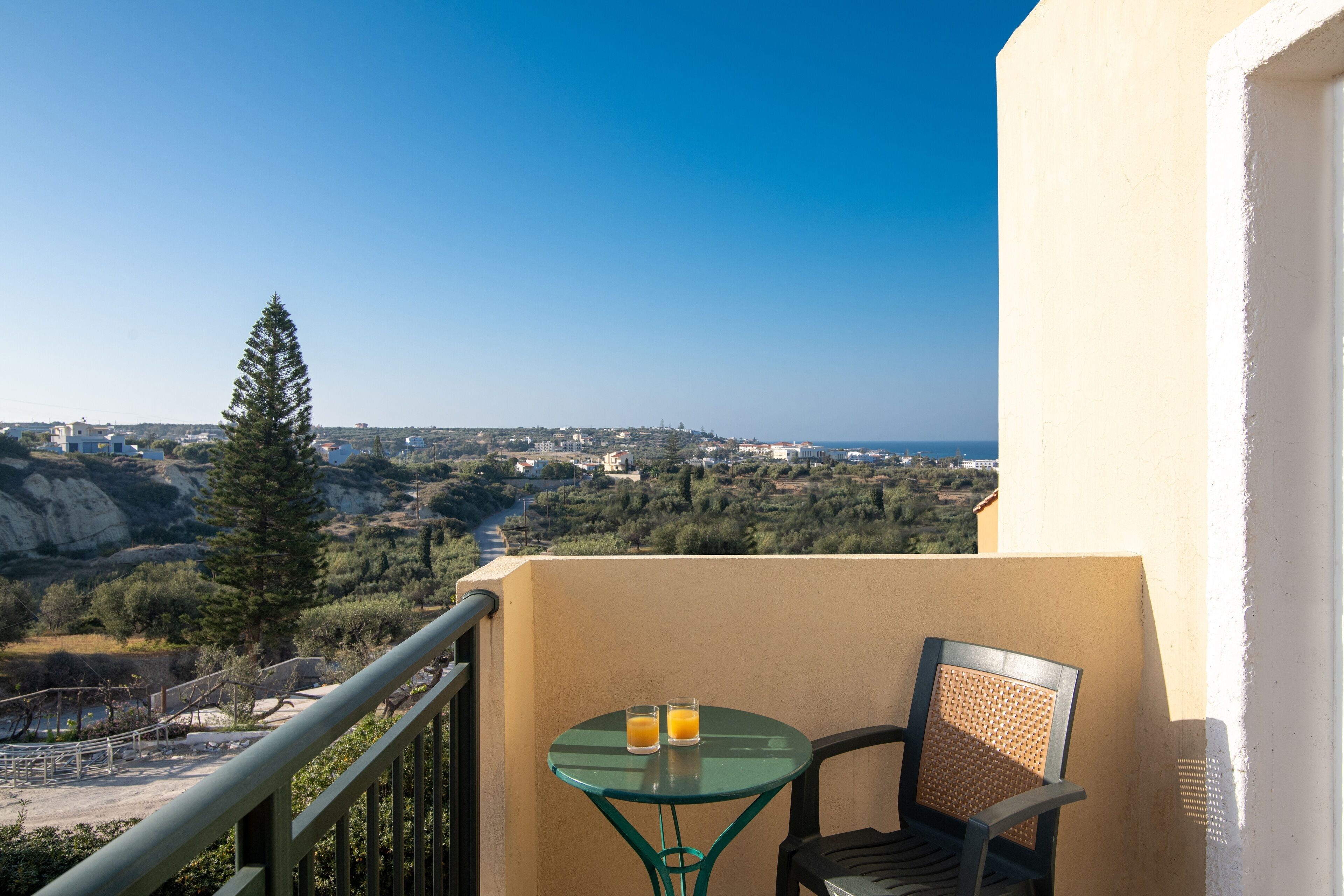 Un balcon avec une table et une chaise, donnant sur un paysage pittoresque, avec des arbres et des bâtiments.
