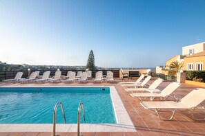 A rooftop pool with clear blue water, surrounded by white lounge chairs and a view of the sea and distant buildings. - Golden Valentin Apartments (Hersonissos)