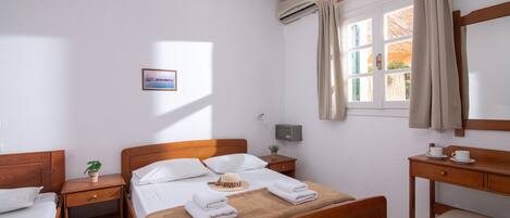 Habitación de hotel con cama de madera, un escritorio, una silla, una mesita de noche, una planta en maceta y una ventana con cortinas.