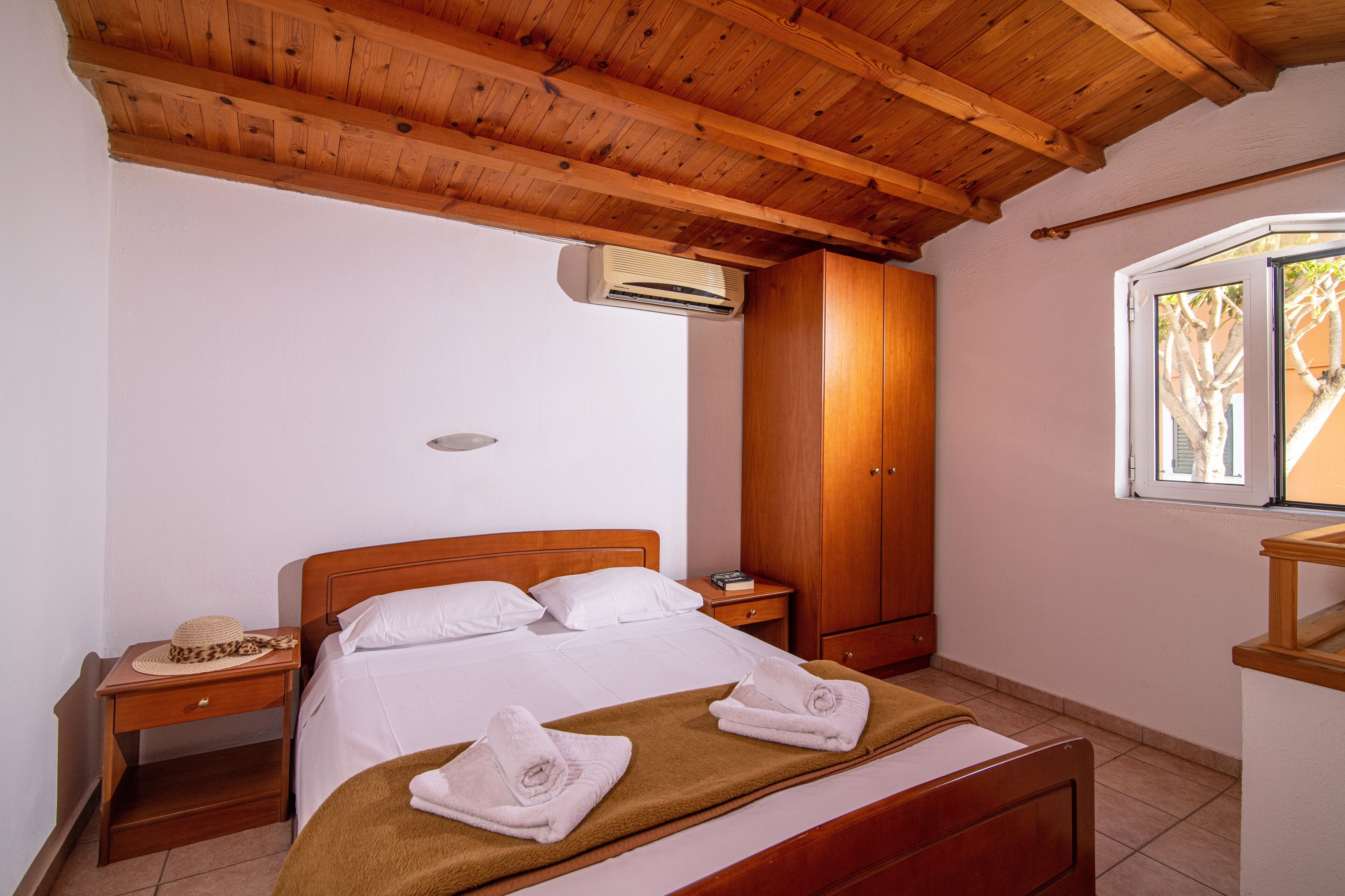 Une chambre avec un plafond en bois, un lit avec du linge de lit blanc, une armoire en bois et un appareil de climatisation.