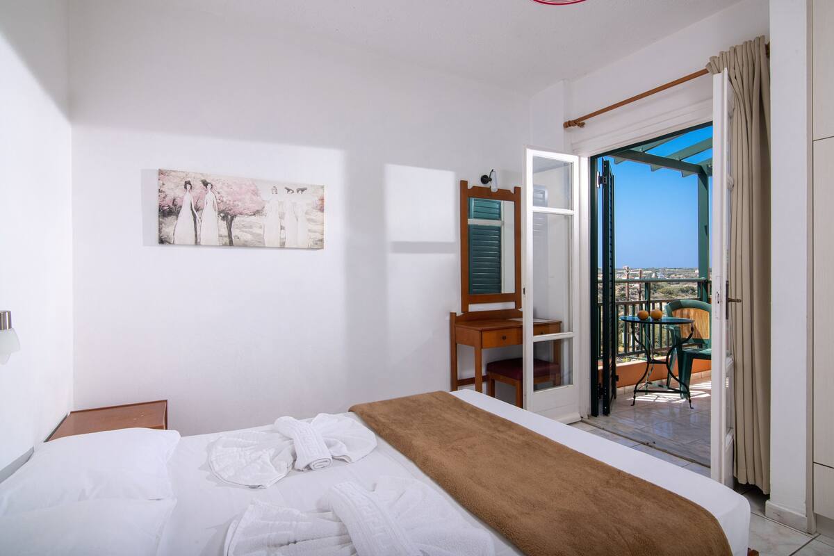 Una habitación de hotel con cama, un cuadro, un escritorio con silla y un balcón con vistas.