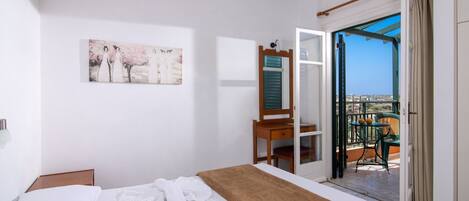 A hotel room with a bed, a painting, a desk with a chair, and a balcony with a view.