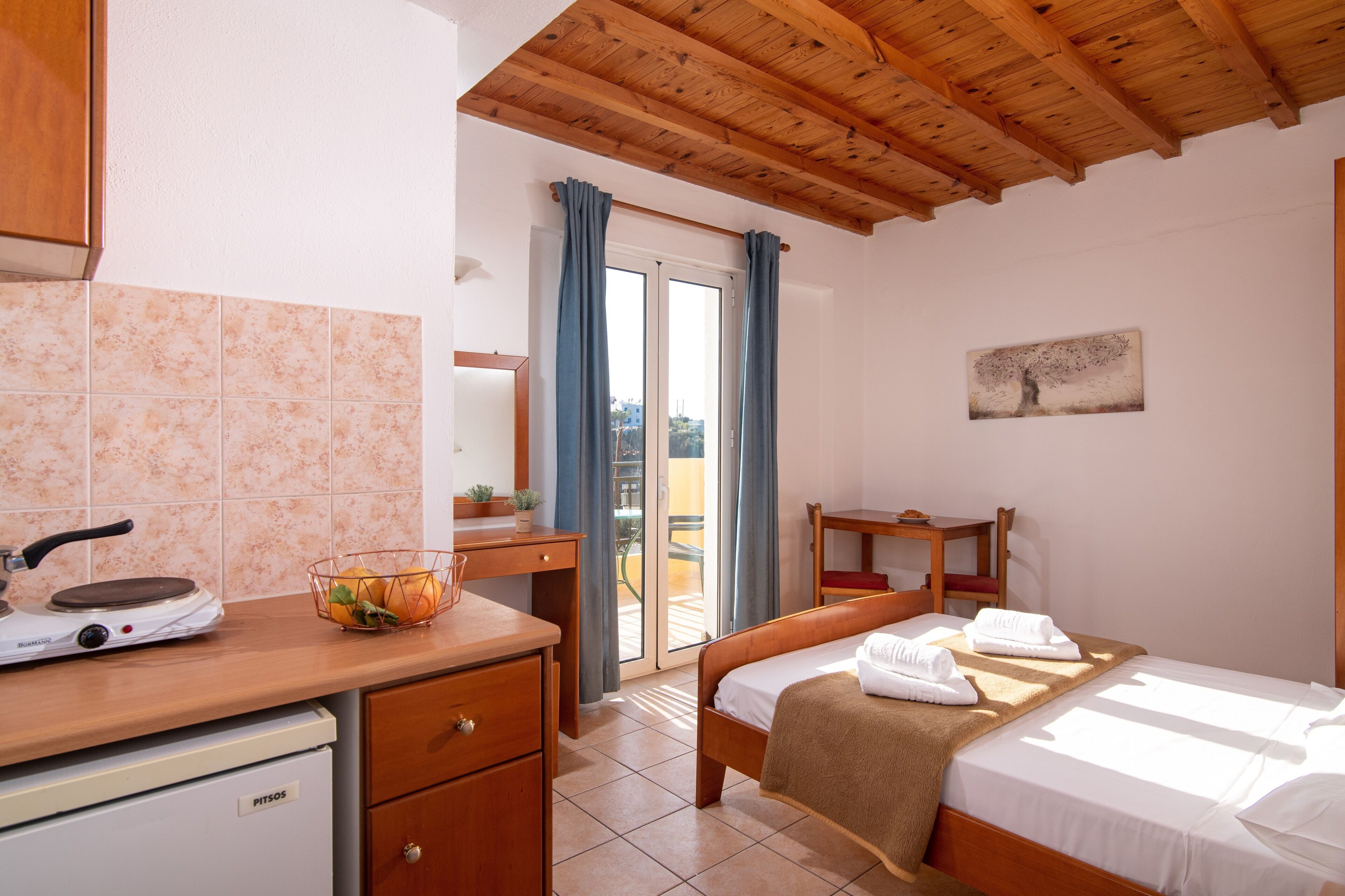 Un dormitorio con cama, escritorio, silla, una mesita, ventana con cortinas y un cuadro en la pared.