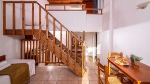 A room with a wooden staircase, a bed, a dining table with breakfast, and a view of the outside. - Golden Valentin Apartments (Hersonissos)
