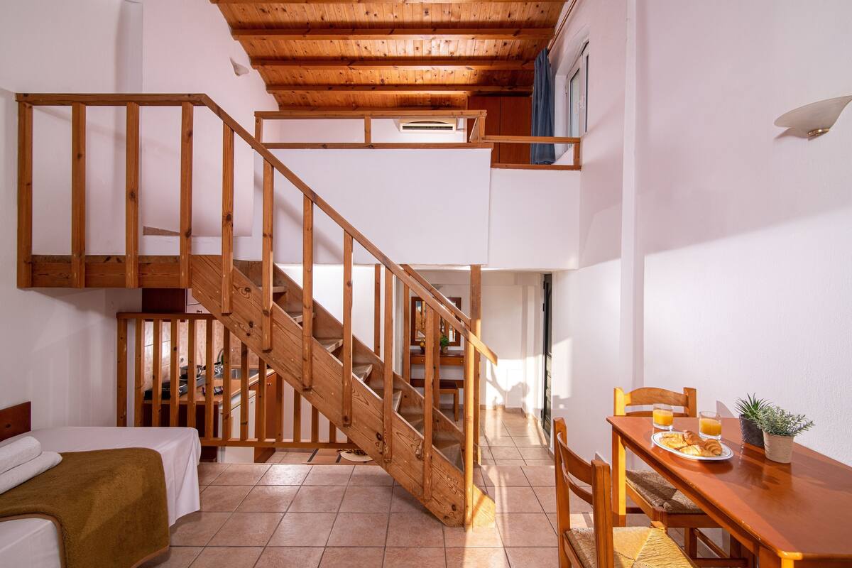 Una habitación con escalera de madera, una cama, una mesa de comedor con desayuno y vistas al exterior.