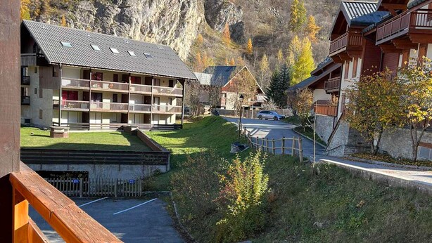 A mountain lodge with a wooden exterior, multiple balconies, and a view of a road leading into the valley. - Charming south-facing studio, 4 pers, balcony in Valloire (Valloire)