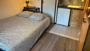 A compact bedroom with a bed, bedside lamp, and a small kitchenette with a sink and cabinets. - Charming south-facing studio, 4 pers, balcony in Valloire (Valloire)
