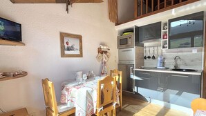 A cozy dining area with a wooden table set for four, a ceiling fan, and a kitchen with modern appliances. - Alcove studio for 3 with terrace near slopes and parking in Praz-sur-Arly (Praz-sur-Arly)