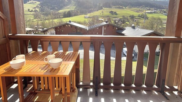 A wooden balcony with a table and chairs, overlooking a mountainous landscape with houses. - Alcove studio for 3 with terrace near slopes and parking in Praz-sur-Arly (Praz-sur-Arly)