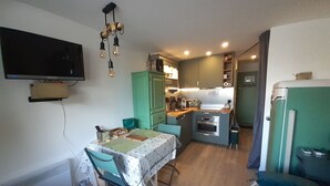 A compact kitchen with a dining table, chairs, a television mounted on the wall, and a vintage refrigerator. - Renovated studio in Valfréjus, near cable car and shops (Valfréjus)