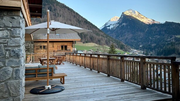 A wooden deck with outdoor furniture, a stone wall, and a mountain view. - Modern chalet in Morzine, 12 pers, 5 br, near center (Morzine)