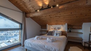 A bedroom with a wooden ceiling, a large bed, a window with a view of a snowy landscape, and a white fur rug. - Modern chalet in Morzine, 12 pers, 5 br, near center (Morzine)